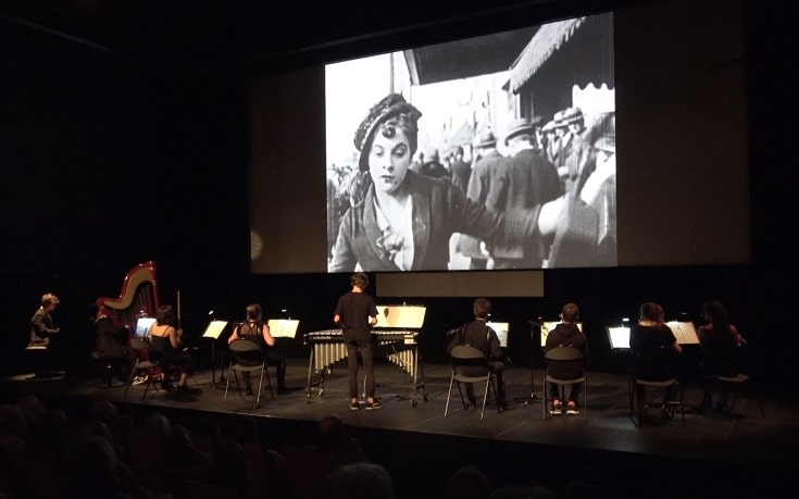 Concert dans le cadre du Festival La Rochelle Cinéma 2019, avec un orchestre philharmonique de dos sur un scène de cinéma en train de jouer devant la diffusion d'un film sur l'écran